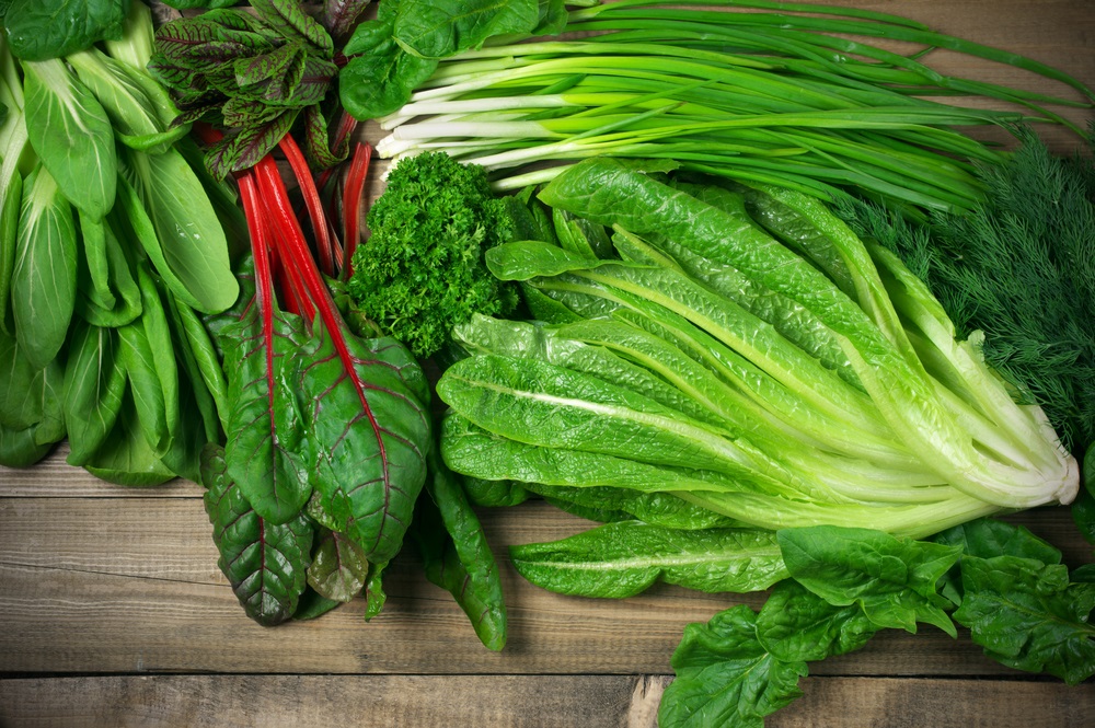 Various green leafy vegetables on wooden table
